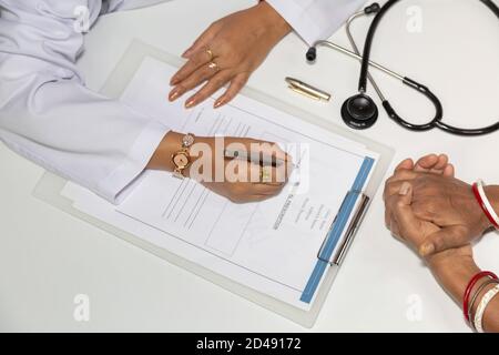 Indische Ärztin schreibt ein Rezept, während ein Patient wartet Mit gepackten Händen in einer Klinik` Stockfoto